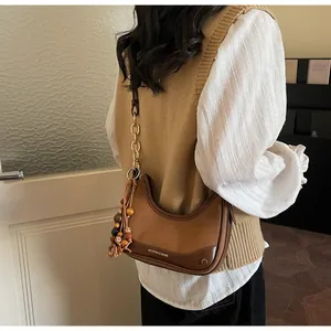 Detail of a brown patchwork crescent bag featuring a stylish chain strap and beaded tassel