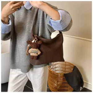 Detail of a brown woven tote bag with a small plush bear charm on minimalist strap