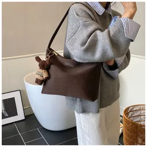Detail of a brown woven bucket bag featuring a cute teddy bear plush charm and leather strap