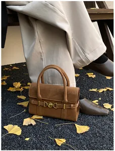 Dettaglio della borsa in pelle scamosciata marrone con fibbia dorata su foglie di ginkgo