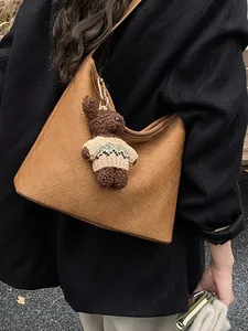 Brown woven leather tote bag with a cute teddy bear charm on a black textured coat