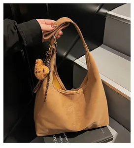 Detail van de kameelkleurige suède hobo tas met teddybeer hanger en gestreept koord