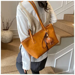 Dettaglio della borsa tote color caramello con ciondolo, indossata come borsa sottobraccio