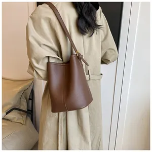 Détail d'un sac seau en cuir grainé marron foncé porté avec un trench-coat beige élégant