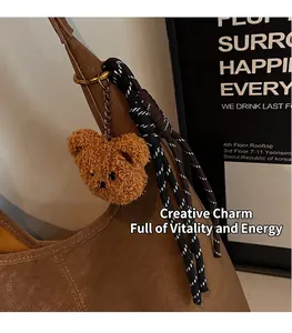 Detail eines braunen Plüschbär-Anhängers mit Goldkette und Kordel an einer Ledertasche