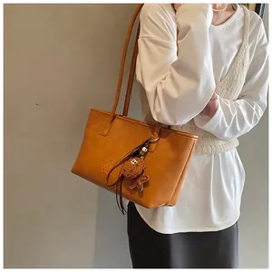 Dettaglio borsa tote in pelle PU marrone con testo goffrato e ciondolo peluche