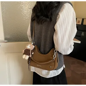 Detail der braunen halbmondförmigen Tasche mit Silberkette und Plüschbär-Anhänger