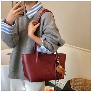 Dettaglio della borsa tote in pelle bordeaux con logo in rilievo e ciondolo a orsetto