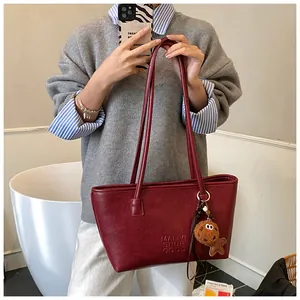 Dettaglio della borsa tote rosso scuro con testo in rilievo e ciondolo a pallina
