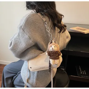 Detail der beigen Umhängetasche mit silberner Kette und süßem Teddybär-Anhänger