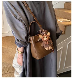 Detail of dark brown lychee leather bucket bag with metal lock and cute bear charm