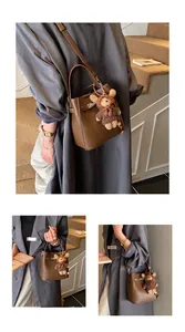 Detail of brown litchi pattern bucket bag with metal buckle and cute bear charm