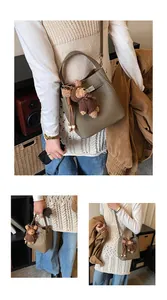 Detail of grey lychee leather bucket bag with metal lock and a cute bear charm