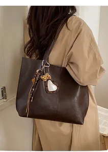 Detail of dark brown tote bag with leopard heart charm and ribbon on model shoulder
