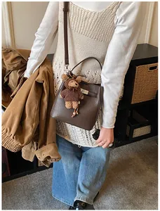 Close-up of brown lychee grain leather bucket bag with silver clasp and cute bear charm