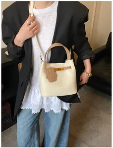 Detail view of cream bucket bag with lychee texture, golden buckle and brown bear charm