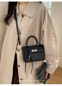 Detail der schwarzen Ledertasche mit Silberschnalle und Anhänger auf beige Trenchcoat