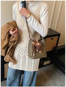 Detail of grey-green lychee leather bucket bag with cute brown plush bear pendant