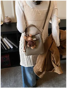 Detail of lychee pattern leather bucket bag in elephant grey with cute teddy bear charm