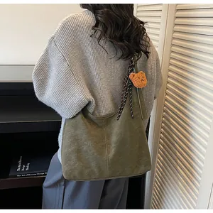 Detail van donkergroene suède hobo tas met decoratief lint en pluche beer bedeltje