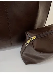 Close-up of deep brown leather texture and golden metal zipper on tote bag