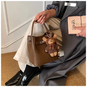 Detail of brown litchi pattern leather bucket bag with a cute bear charm pendant