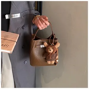Detailed shot of brown lychee grain bucket bag featuring a cute plush bear pendant accessory