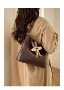 Detail der dunkelbraunen Hobo-Tasche aus Leder mit Hasenanhänger am beigen Trenchcoat