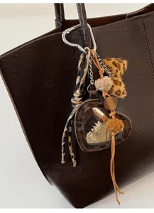 Detail of leopard print bag charm featuring heart mirror and plush pom-poms on a leather tote
