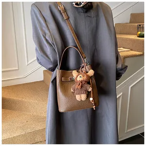 Detailed view of a brown pebbled leather bucket bag featuring a cute teddy bear charm