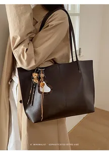 Detailed side view of a large brown retro tote bag with heart charm and plush ball accessory