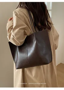 Deep brown oversized tote bag with vertical stitching shown on a model in trench coat