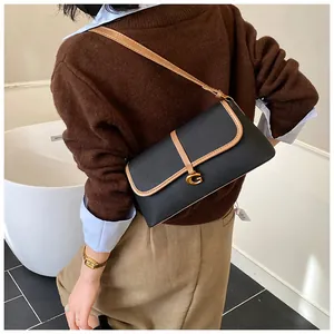 Détail d'un sac en cuir noir avec bordure marron et boucle dorée en G sur la bandoulière