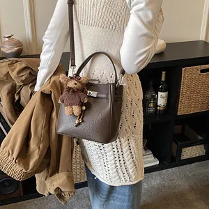 Brown lychee leather bucket bag with metal lock and cute teddy bear charm on model