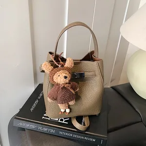 Chic khaki pebbled leather bucket bag with cute bear charm on a designer book base