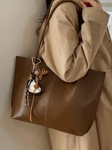 Large dark brown leather tote bag with decorative charms worn by a model in a trench coat