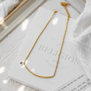 Macro detail of gold-plated beaded chain with curved bar and sparkling zircon stone