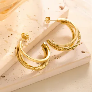 Details von goldenen geometrischen Doppel-Ohrringen mit Gittermuster auf Steinplatte