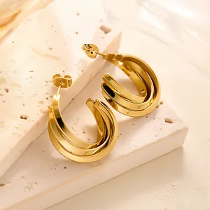 Detailansicht der mehrlagigen C-förmigen Creolen in Gold auf einer strukturierten Steinfläche