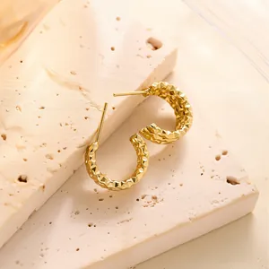 Detailansicht goldener C-förmiger Ohrringe mit Diamantschliff-Textur auf Stein