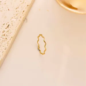 Nahaufnahme eines minimalistischen goldenen Wellenrings aus Titanstahl auf Marmoroberfläche