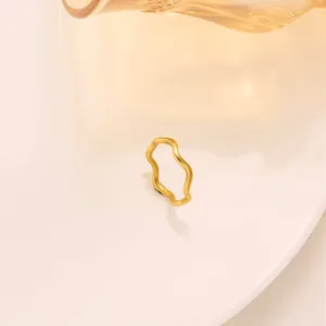 Makroaufnahme eines minimalistischen goldenen Wellenrings aus Edelstahl auf warmem Grund