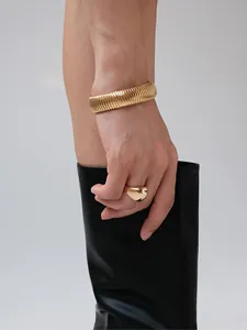 Dettaglio macro del bracciale dorato a coste e anello a goccia lucido su modella