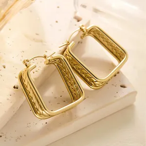 Detailaufnahme goldener geometrischer Ohrringe mit Weizenmuster auf beigem Naturstein