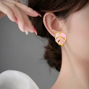 Boucles d'oreilles feuilles roses avec bordure dorée portées par un mannequin de près