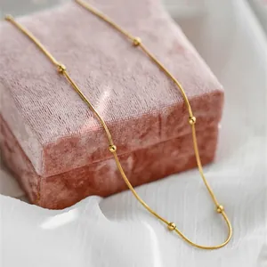 Vergoldete Schlangenkette mit kleinen Perlen auf rosa Samt und weichem Tüll-Hintergrund