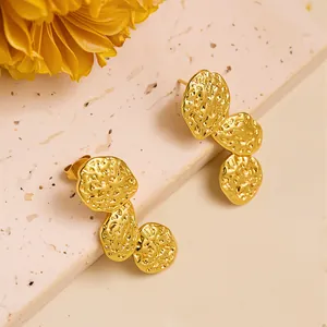 Detailed view of gold leaf flower earrings with hammered texture on beige stone stand