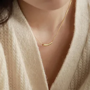 Collier minimaliste en titane doré avec pendentif aubergine porté sur un pull en maille beige