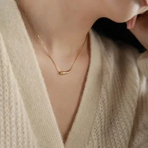 Gros plan d'un collier pendentif haricot doré sur un pull en maille beige pour femme