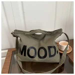 Vista dettagliata della borsa a tracolla in tela verde militare con stampa MOOD su legno